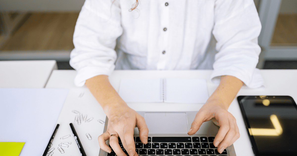Vista superior de una persona autónoma tecleando en su ordenador portátil sobre un escritorio blanco de oficina para solicitar su certificado digital.