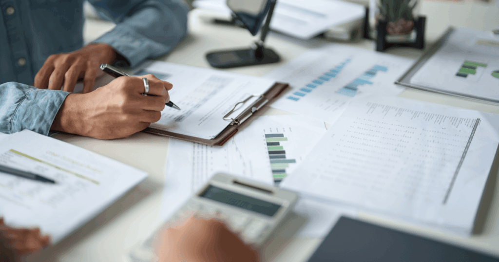 rimer plano de unas manos revisando informes financieros, gráficos de facturación y usando una calculadora sobre un escritorio de oficina.