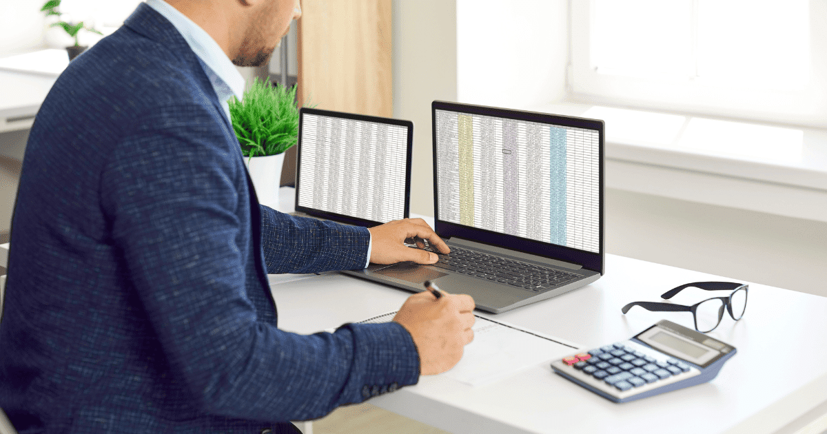 Un autónomo trabajando en su oficina con un ordenador portátil, una pantalla secundaria con gráficos de Excel y una calculadora.