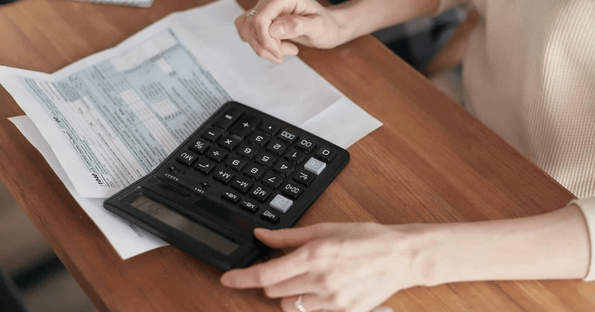 Manos de un contribuyente utilizando una calculadora negra sobre una mesa de madera para calcular cómo fraccionar pago renta.