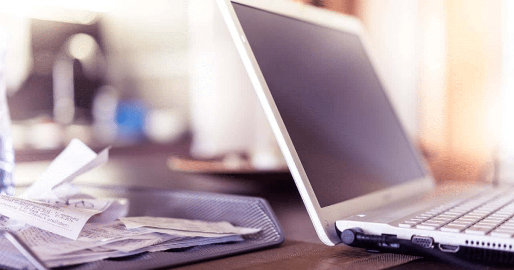 Bandeja de oficina llena de tiques y recibos acumulados junto a un ordenador portátil, representando la duda de un autónomo sobre cuanto tiempo tengo para deducir el iva de una factura antes de que caduque el plazo legal.