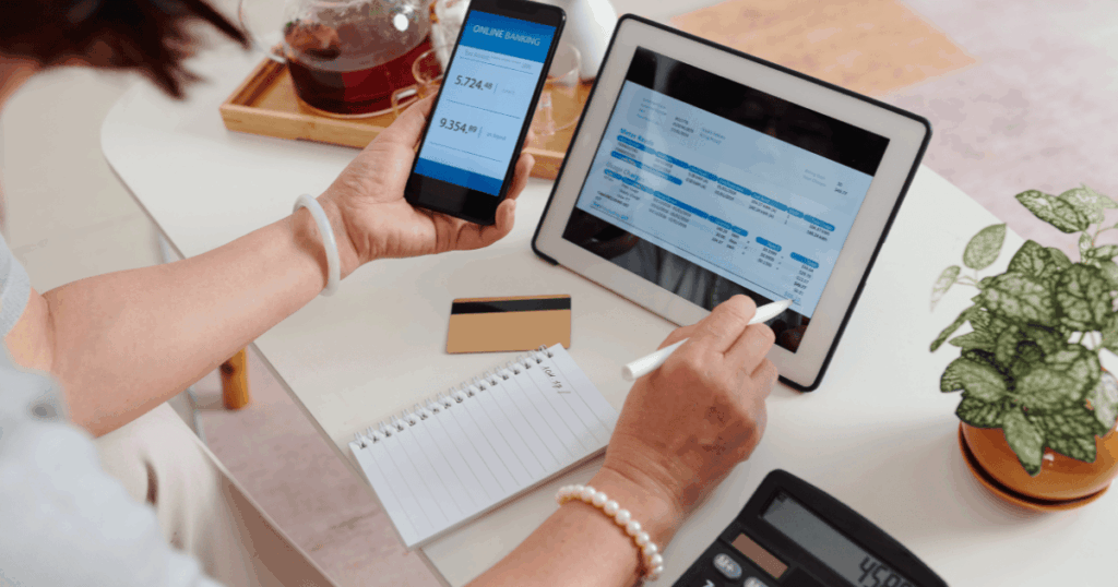 Una autónoma revisa la aplicación de banca online en su móvil y comprueba los datos de una factura digital en su tablet con un puntero para asegurarse de no emitir una factura con fecha anterior o posterior.